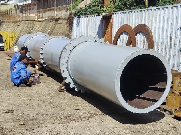 Workers painting large kiln pipe at fabrication workshop in Batam